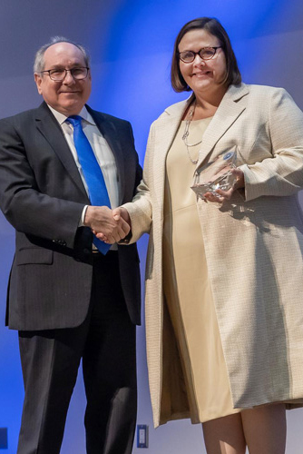 Dr. Podolsky, shaking hands with Dr. Rogers, smiling woman brown hair, wearing a beige dress and jacket, holding her award.
