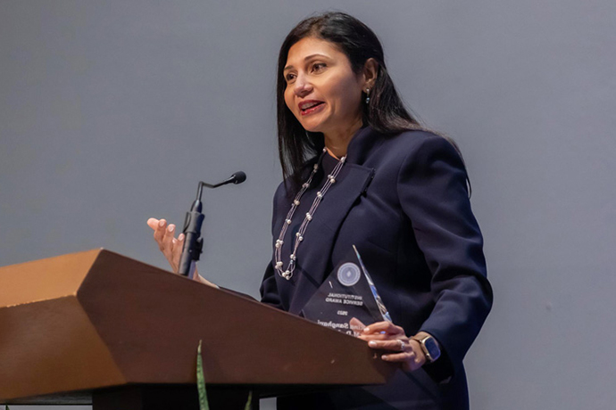 Dr. Sanghavi, woman with long dark hair wearing a dark jacket, standing behind a podium holding her award.