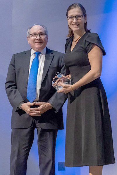Dr. Podolsky standing with Dr. Voit, smiling woman with long dark hair wearing a brown dress, holding her award.