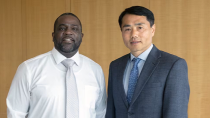 Two men standing together in front of a paneled wall. 