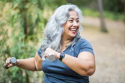 Smiling woman with long gray hair, walking for exercise, holding weights.