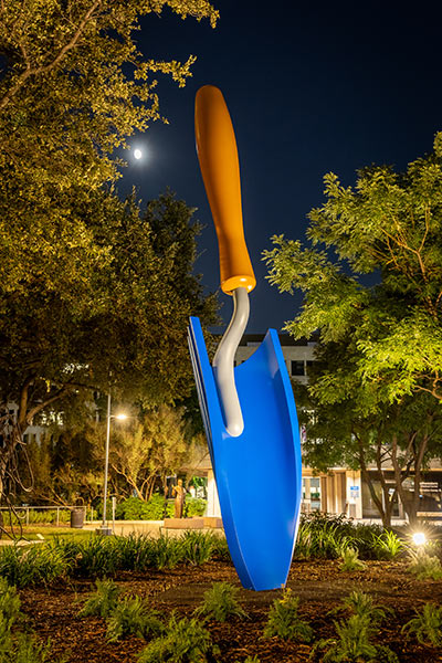 Large blue-bladed trowel sculpture at night, front view