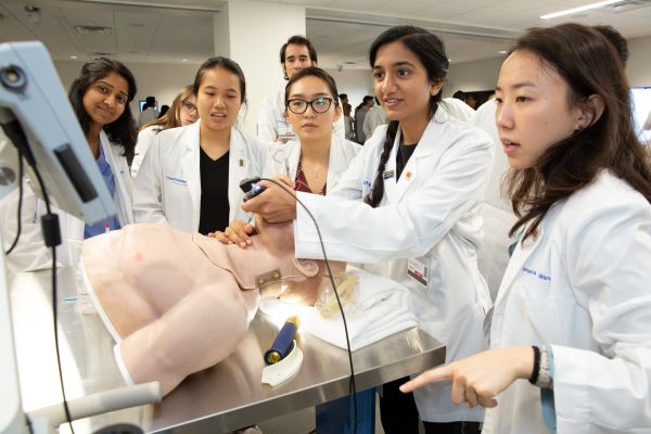 group of medical students gather around medical manikin to practice inserting airway tube