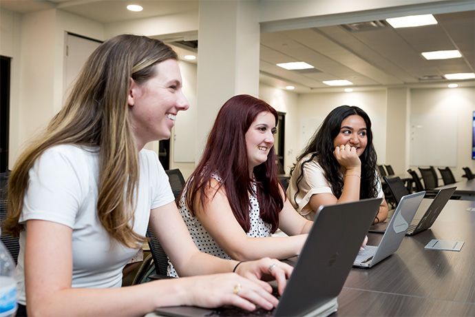 Three smiling female students watching the lecturer and typing on their laptop computers.