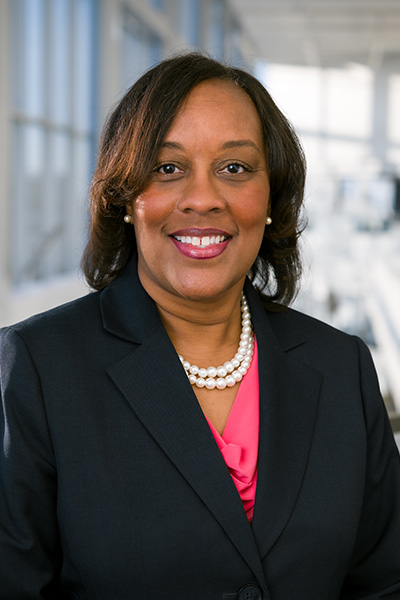 headshot of Dr. Carolyn Bradley-Guidry; black woman wearing black jacket and bright pink shirt with short double pearl necklace