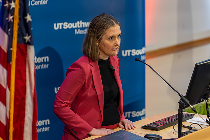 Jessica Spaniol, J.D., speaks at podium in front of UT Southwestern backdrop and American flag