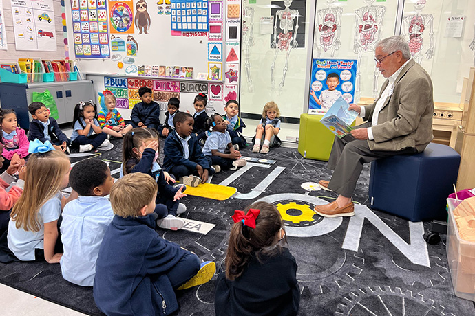Dr. Charles Ginsberg sits and reads to young students at UTSW Biomedical Preparatory