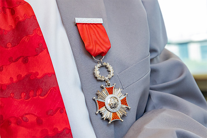 Red and silver medal suspended from a red ribbon on the lapel of a gray suit to the right of a white shirt and red tie.