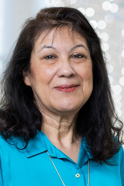 Smiling woman with long dark hair, wearing a bright blue blouse and gold necklace.