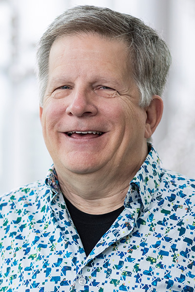 Smiling man with short gray hair, wearing a blue and white print shirt.