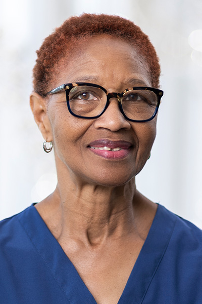 Smiling woman with short red hair, wearing blue UT Southwestern scrubs an black glasses.