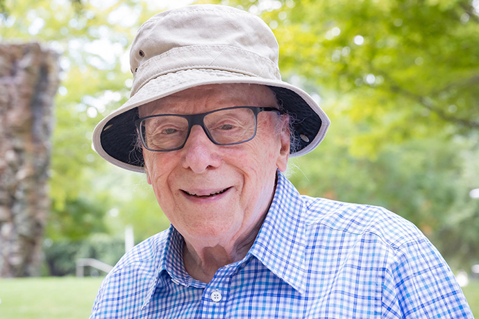 Dr. Goldstein wearing a blue checked shirt, tan hat and dark-rimmed glasses.