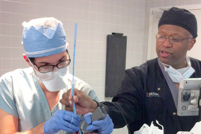 medical student on left practices installing breathing tube on OR patient as older black doctor supervises