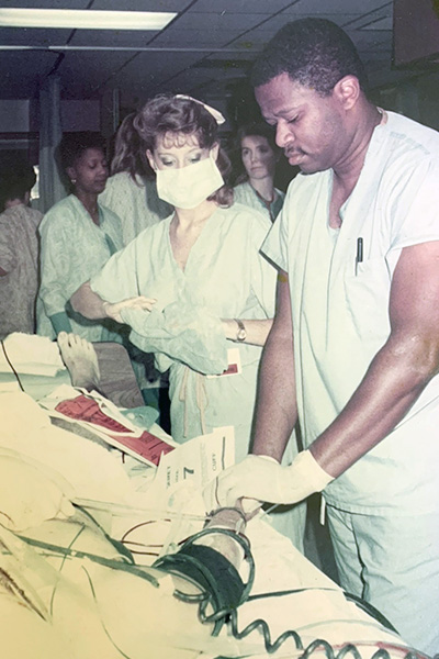 black male doctor stands next to a patient on a gurney with other medical staff surrounding