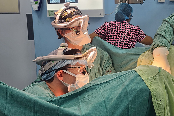 Two doctor wearing surgical gear performing surgery on a sheeted patient.