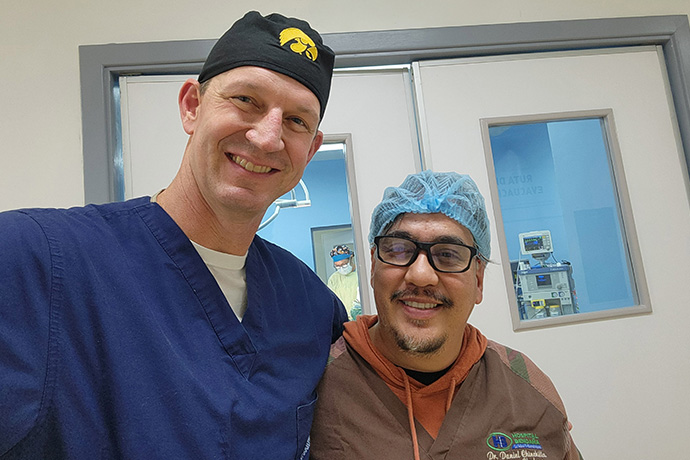 Two men in surgical scrubs standing outside operating room doors.