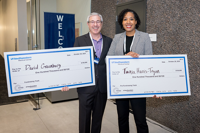 Two smiling people holding over-sized checks for their winnings. David Greenberg, left, $100,000, Tania Harris-Tryon, right, $100,000.