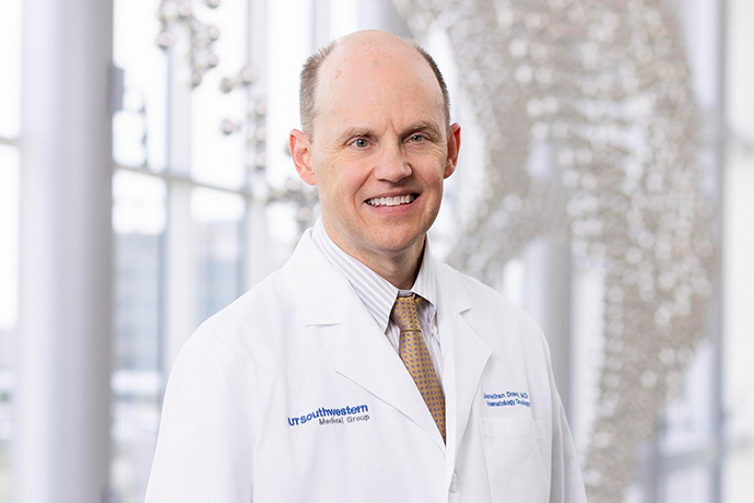 Smiling man with receding hair, wearing a white UT Southwestern Medical Center lab coat.