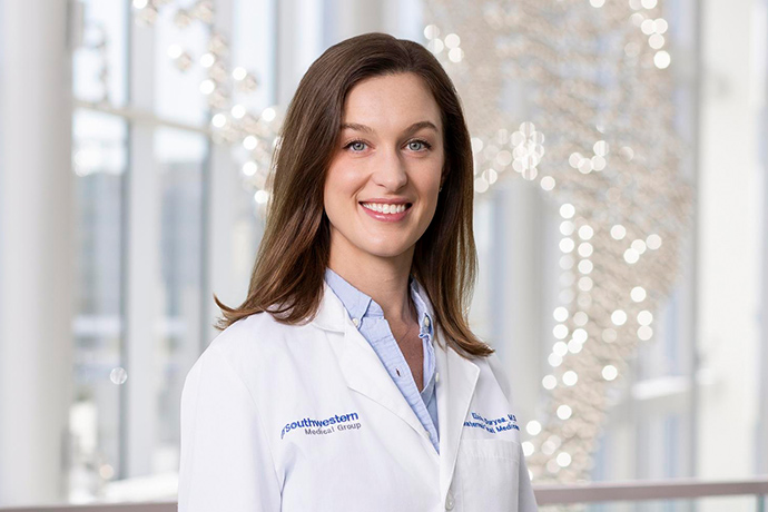 Smiling woman with long brown hair, wearing a white UT Southwestern Medical Center lab coat.