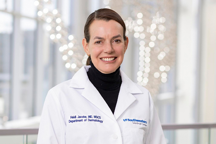 Smiling woman with dark hair pulled back in a ponytail, wearing a white UT Southwestern Medical Center lab coat.