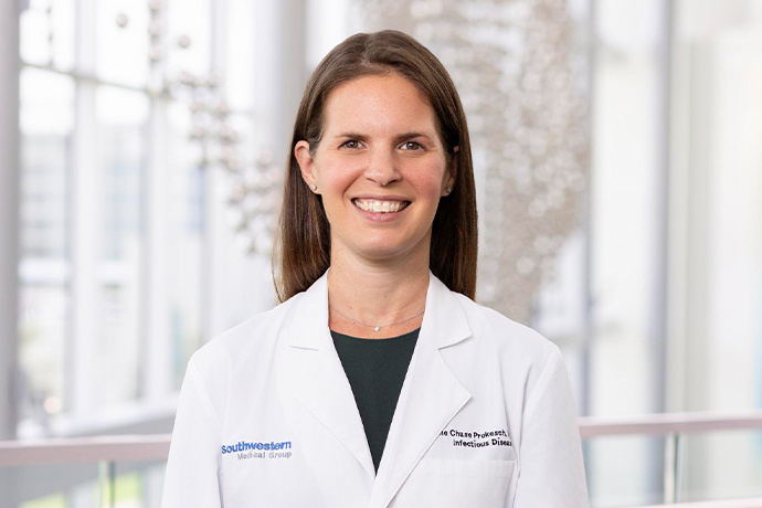 Smiling woman with long brown hair, wearing a white UT Southwestern Medical Center lab coat.