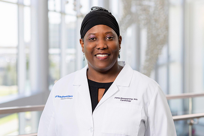 Smiling woman wearing a black cap and a white UT Southwestern Medical Center lab coat.