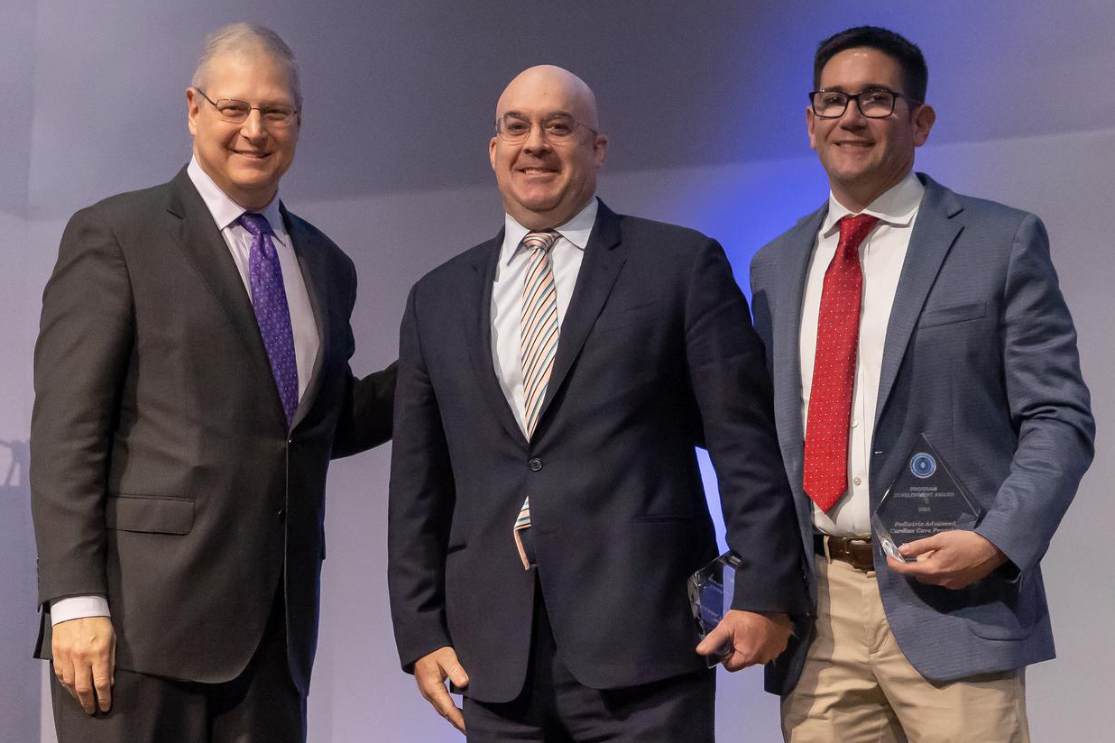 Three men in suits. Two men on the right hold their new award plaques.