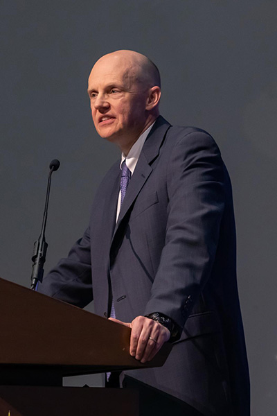 Bald man wearing a dark gray suit speaks from a podium.