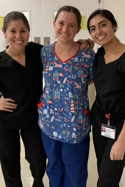 Three women wearing scrubs, standing in a hospital hallway.