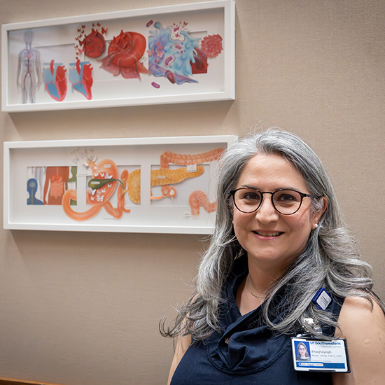 woman with glasses, long silver hair and blue shirt stands in front of her collage artwork in 2 white frames on the wall