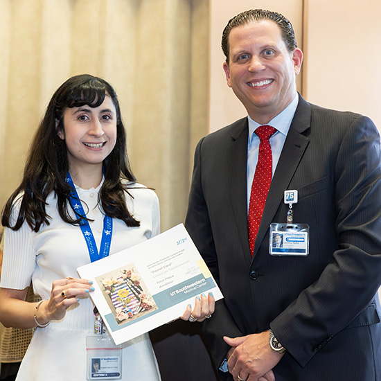 woman with long dark hair at left hold certificate, tall man in grey suit with red tie smiles as the presentation