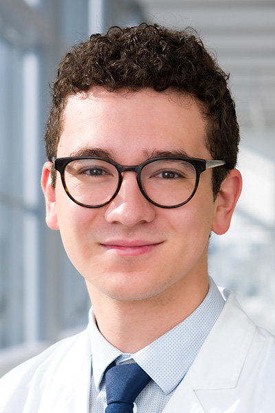 Smiling man with dark hair, wearing a lab coat and glasses.