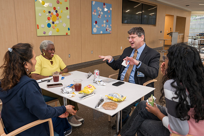 Dr. Efron, a man with wearing a gray suit, gesturing while speaking with three woman. All are seated at a table eating lunch.