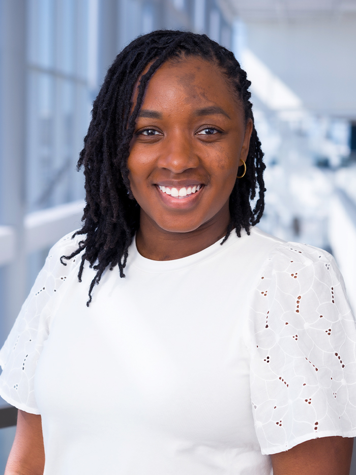 Smiling woman with shoulder length black braids, wearing a white blouse with short eyelet sleeves.