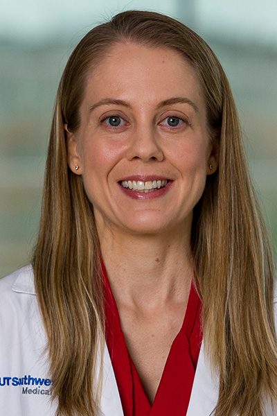 Smiling woman with long light-brown hair wearing a white UT Southwestern Medical Center lab coat over a red blouse.