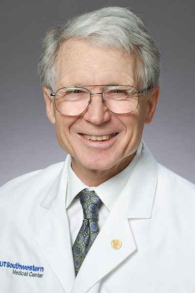 Smiling man with white hair a white UT Southwestern Medical Center lab coat and wire-rimmed glasses.