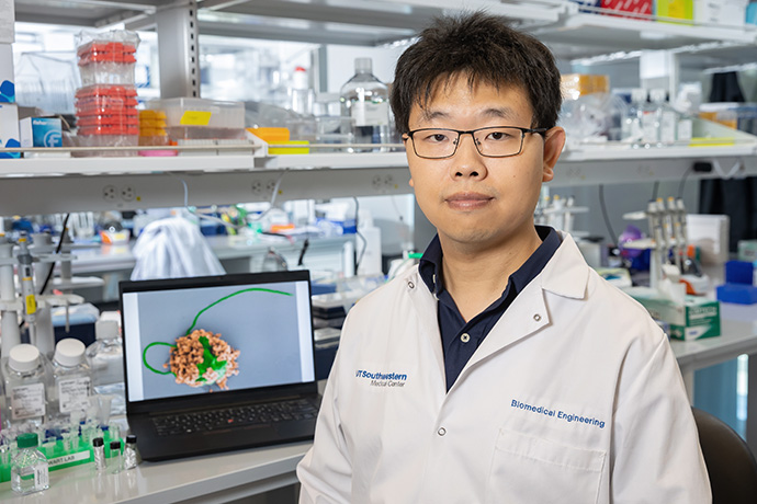 Dr. Fangyu Zhang seated in lab with microbot shown on laptop display behind him