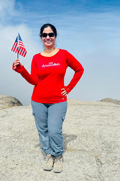 Dr. Vemalapalli stands on the peak above the clouds holding an American flag