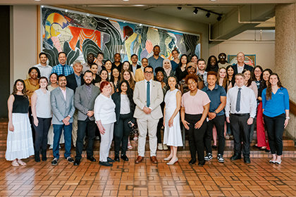 A large group of individuals wearing business casual outfits grouped on terra-cotta steps in front of a large abstract painting.