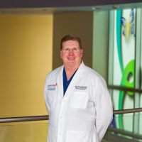 Alan Farrow-Gillespie, M.D., white man in medical coat, posing in front of gold colmumn