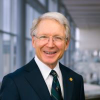 Kevin Klein, M.D., older white man, wearing navy suit jacket, and silver framed glasses, grey hair, smiling