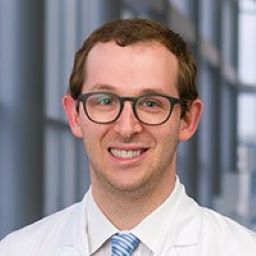 Benjamin Heller, M.D., white man with brown hair, and black glasses, wearing medical coat, smiling