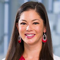 woman with long brown hair, wearing red earrings, smiling, posing at hospital