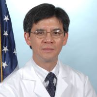 man posed next to united states flag, brown hair, wearing silver glasses