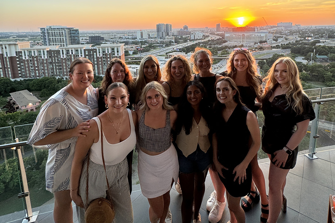 Group of women posing for the camera on a balcony with a cityscape in the background