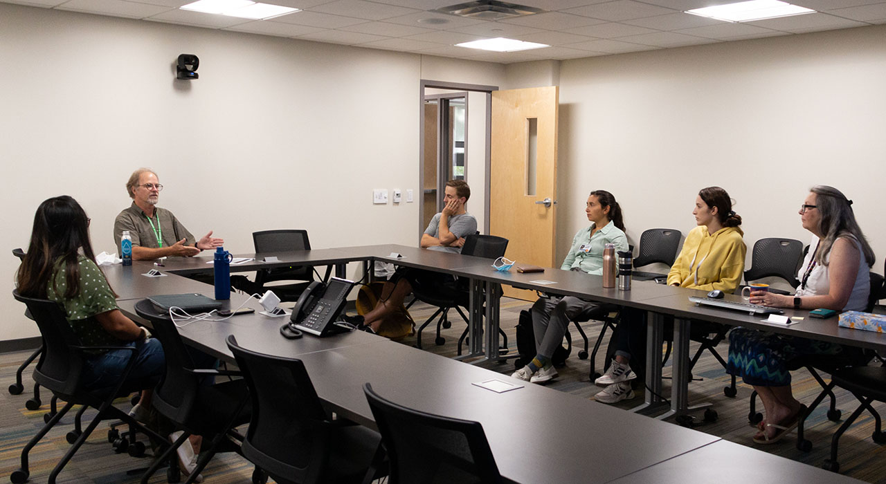 A group of students seated in a conference room listening to a speaker who is seated at the main table