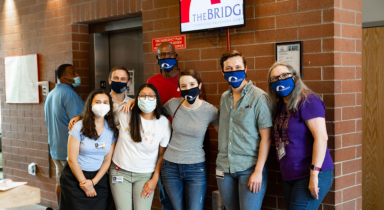 A group of UTSW students with the director of The Bridge Homeless Recovery Center posing for a photo under The Bridge sign