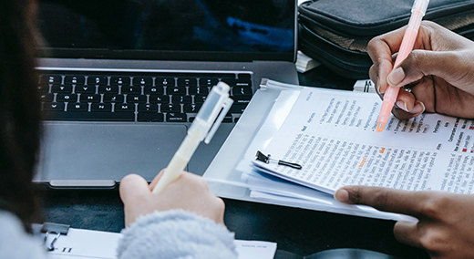 A close-up photo of hands working on a clipboard and on a laptop computer