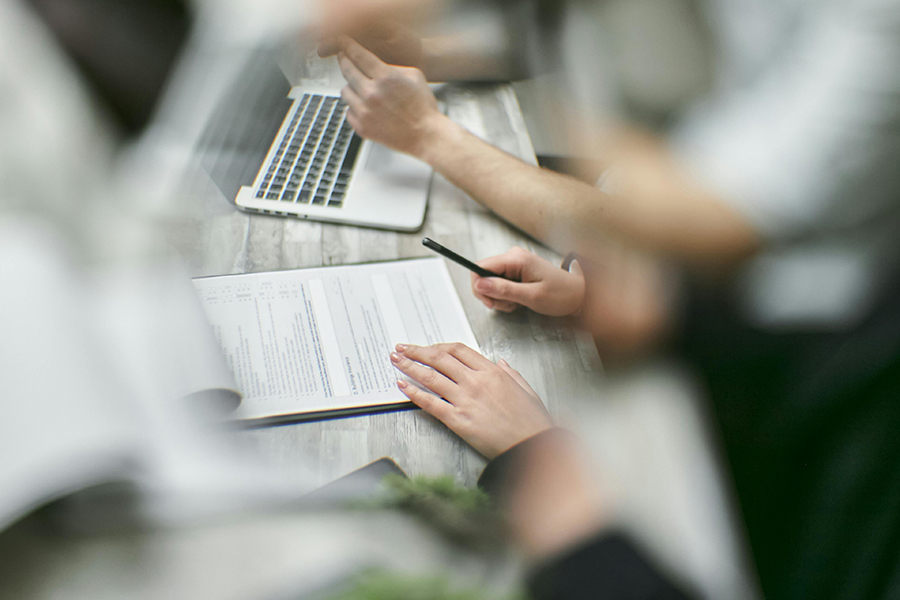 people at a table with a paper form, pen, and laptop computer
