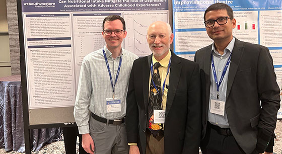 Three men stand in front research posters at a conference